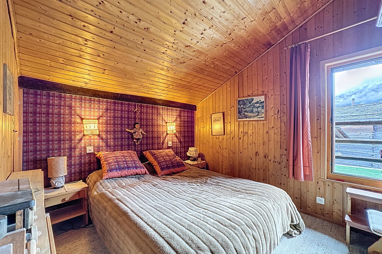 Chambre lambrissée avec lit double, tête de lit en tissu écossais et fenêtre sur la vallée.