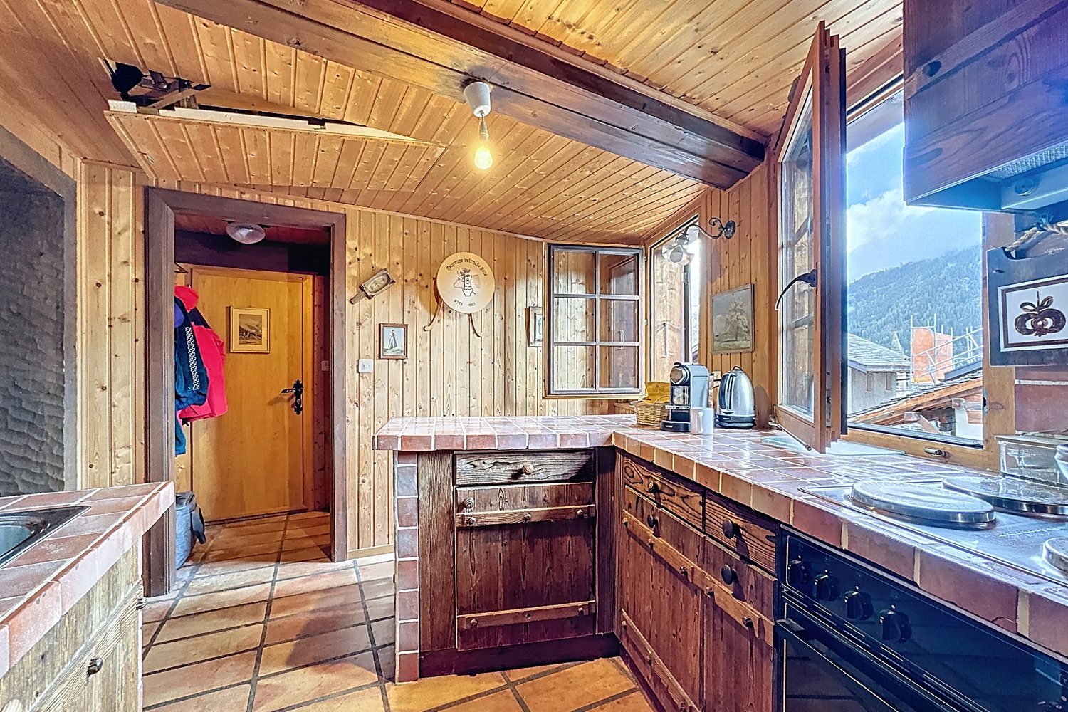 Cuisine équipée avec plan de travail carrelé, meubles en bois, four et fenêtre sur les montagnes.