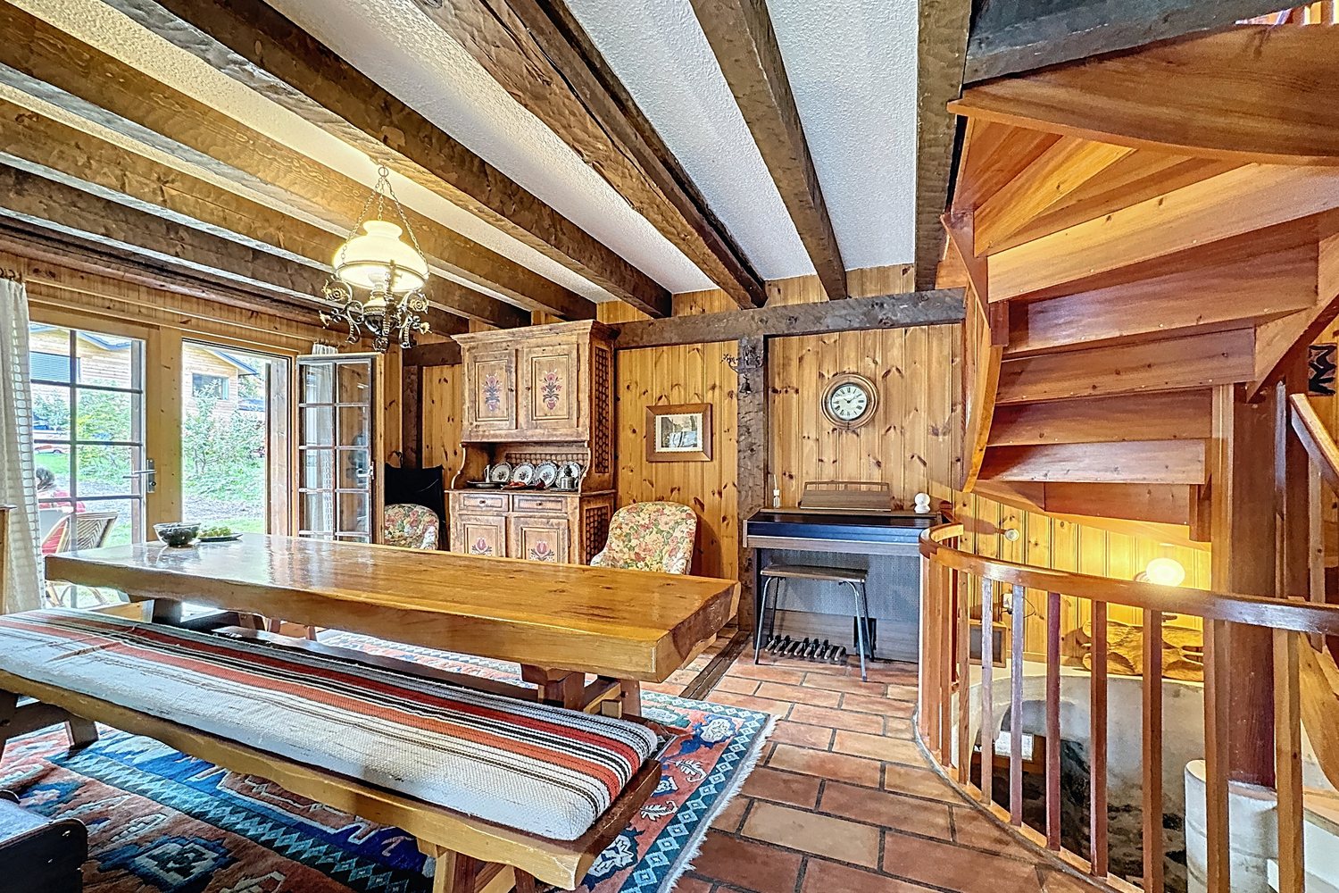 Salle à manger avec grande table en bois massif, banc, buffet ancien et escalier en colimaçon.